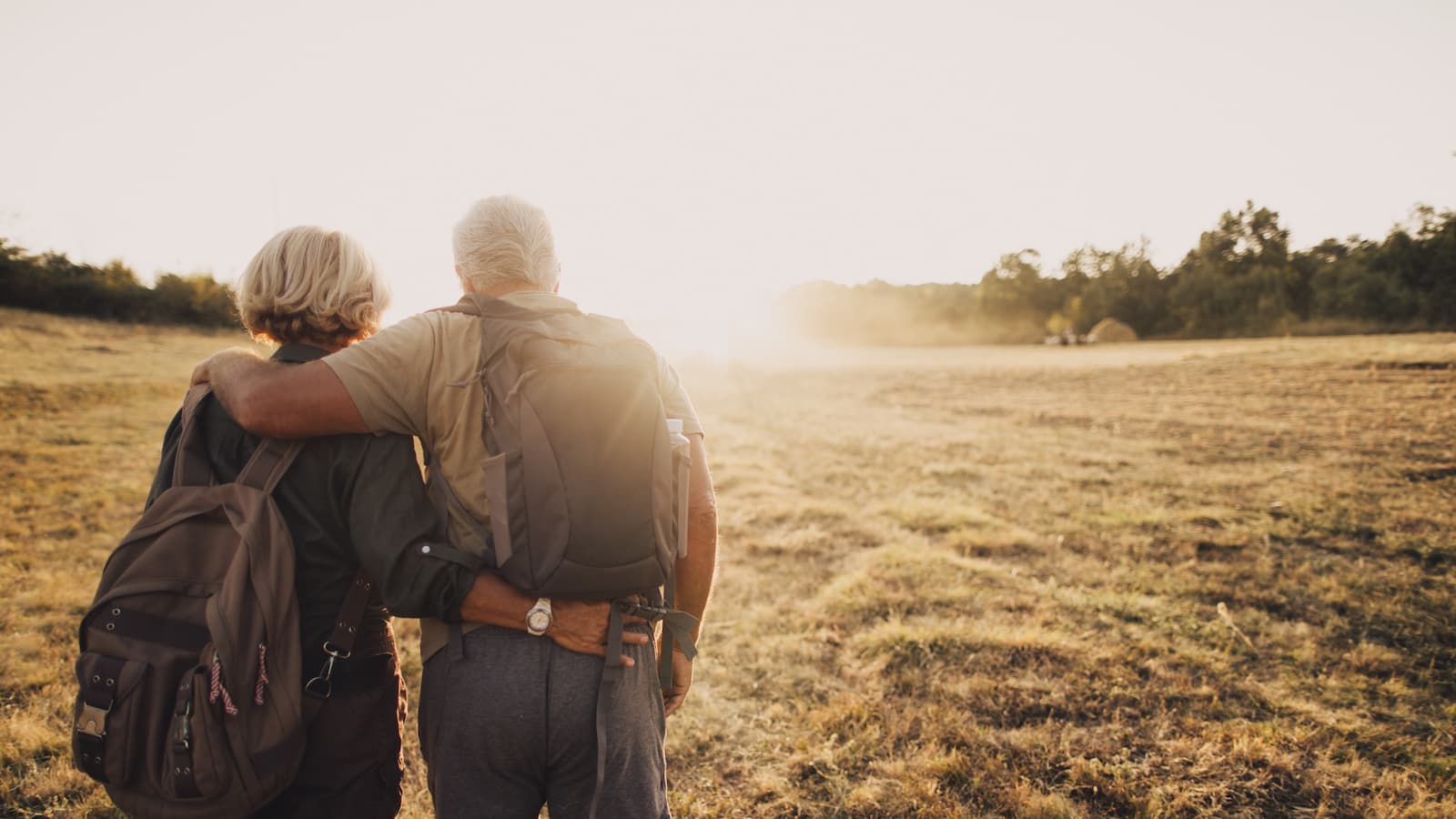 an elderly couple hugging each other and looking at the sunset on a field